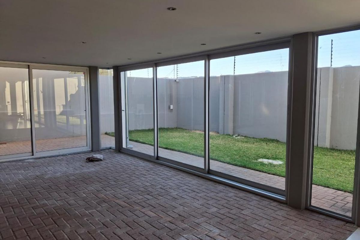 A spacious, empty covered patio featuring large sliding glass doors that open onto a private garden area with paved flooring and recessed lighting.