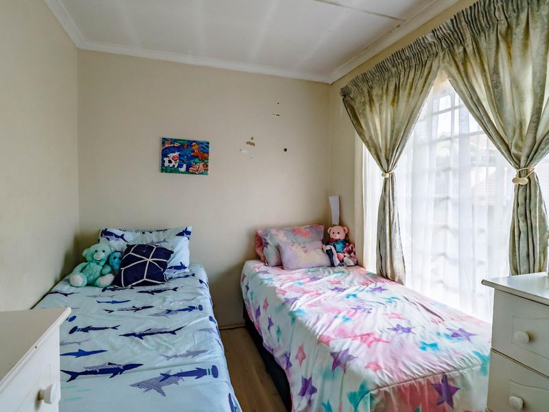 A compact bedroom featuring laminate flooring, a window with security bars, and coved ceilings, requiring minor cosmetic wall repairs.