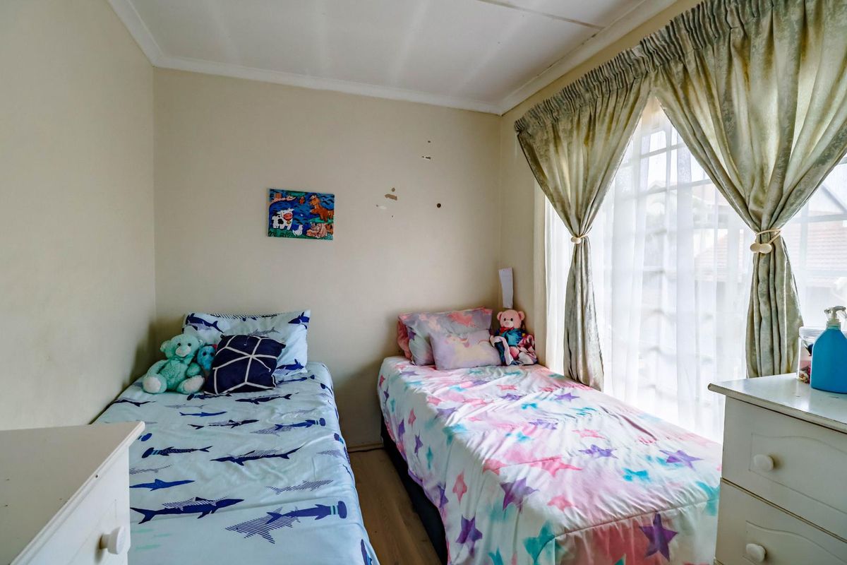 A compact bedroom featuring laminate flooring, a window with security bars, and coved ceilings, requiring minor cosmetic wall repairs.