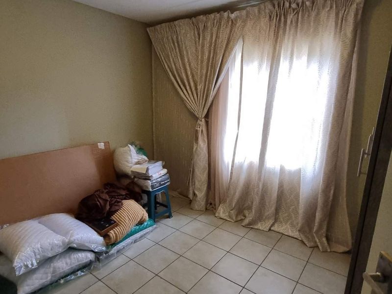 A simple bedroom featuring tiled flooring and window curtains, providing a neutral space ready for personalization.