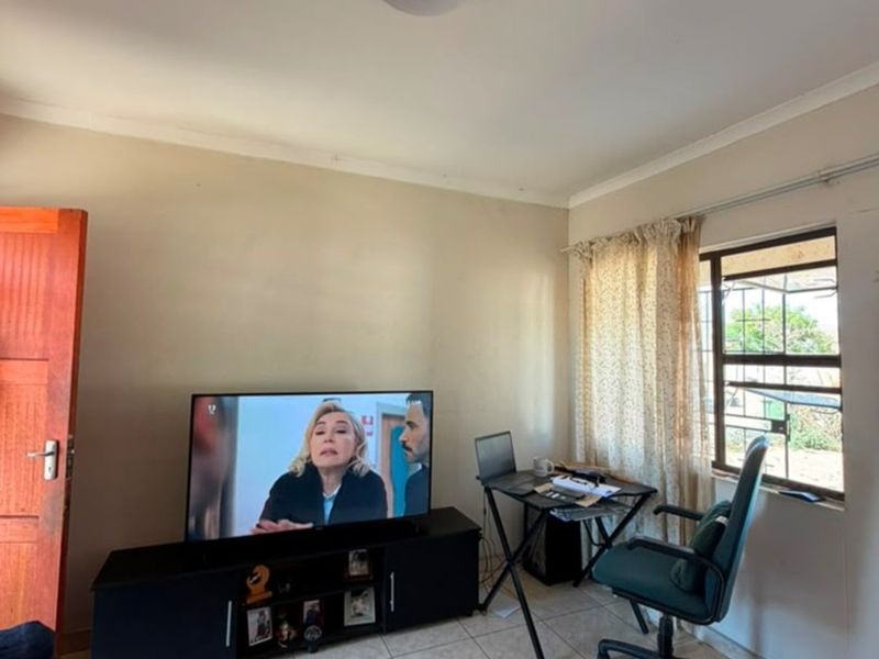 A functional living area featuring tiled flooring, a window with security bars, and coved ceiling detailing.