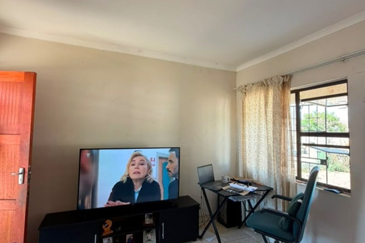 A functional living area featuring tiled flooring, a window with security bars, and coved ceiling detailing.