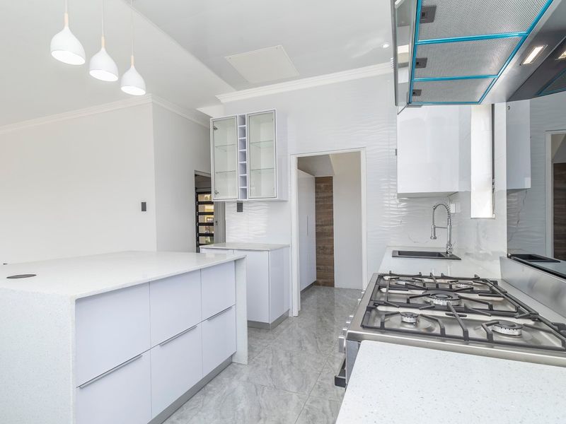 Modern kitchen featuring white cabinetry, stone countertops, a gas cooktop with extractor fan, and a central island, finished with sleek tiled flooring.