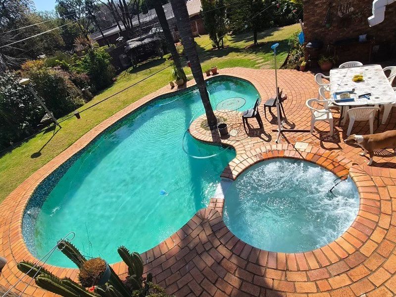 Outdoor entertainment area featuring a kidney-shaped swimming pool with an integrated spa, surrounded by brick paving and a well-maintained garden.