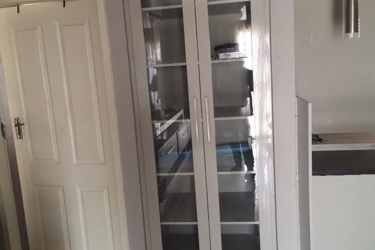Interior view featuring a built-in glass-fronted display cabinet, tiled flooring, and a panelled door within a neutral-toned living space.