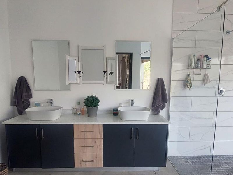 Modern bathroom featuring a double vanity with vessel sinks, built-in cabinetry, and a spacious walk-in shower with marble-look wall tiles.