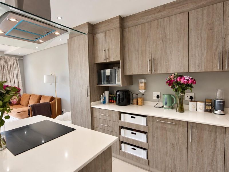 Modern open-plan kitchen featuring wood-look cabinetry, quartz countertops, integrated appliances, and a central island with an induction hob, flowing into the living area.