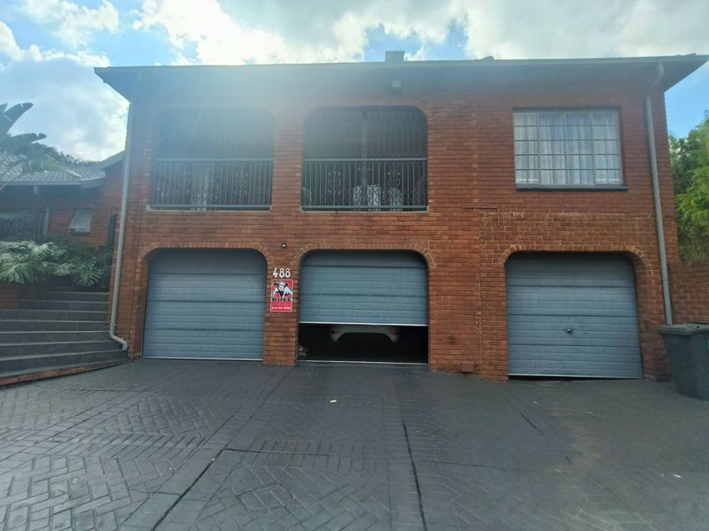 Front elevation of a double-story brick house featuring a triple garage with automated doors and an upper-level balcony with security gates.