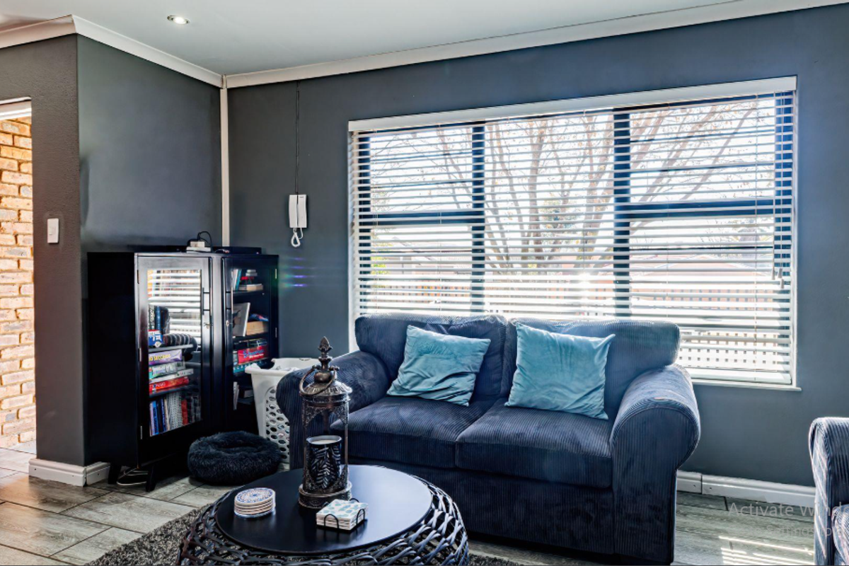 A comfortable living room featuring tiled flooring, dark grey walls, and large windows fitted with venetian blinds, providing ample natural light.
