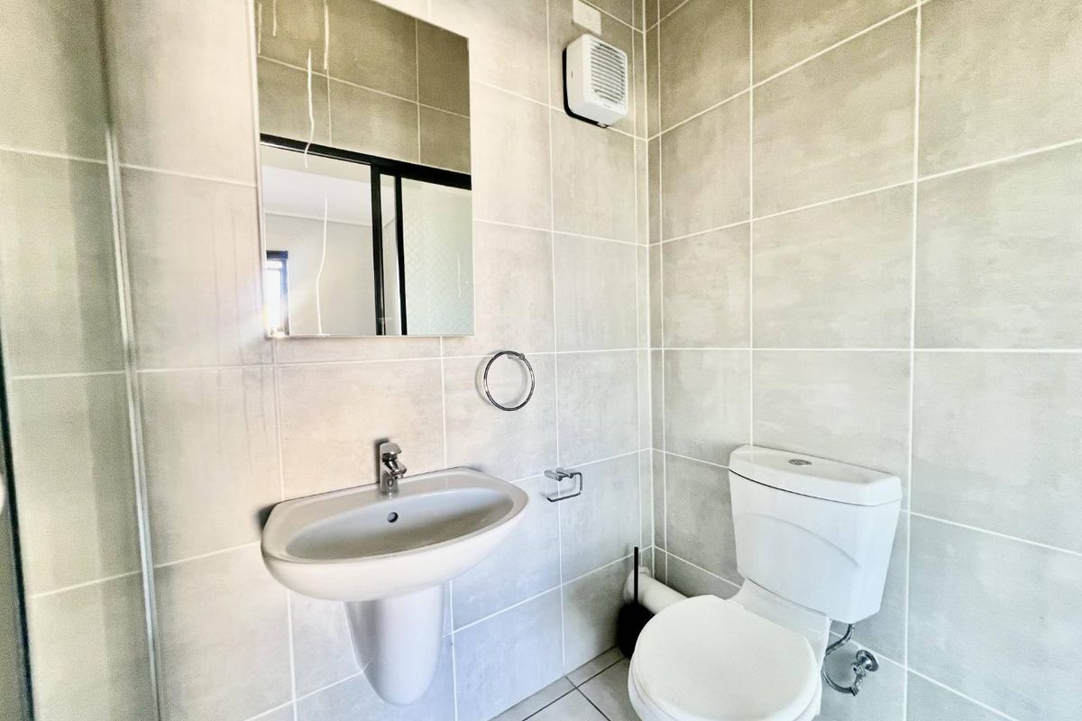 A clean, modern bathroom featuring neutral wall tiles, a wall-mounted basin, and a standard toilet.