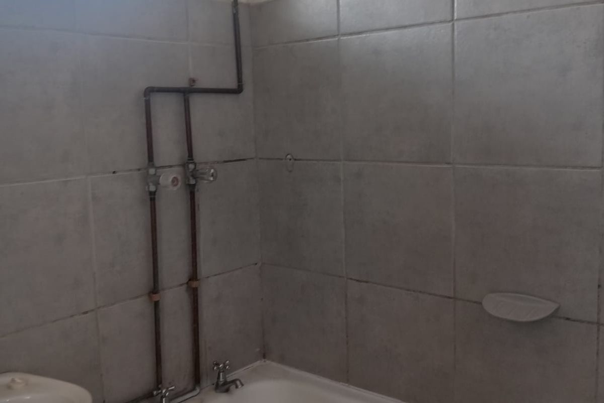 A functional bathroom featuring a bathtub with exposed copper plumbing, tiled walls, and an obscured glass window for privacy.