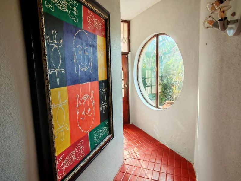 A bright hallway featuring unique terracotta tile flooring, a distinctive circular window, and a wall-mounted light fixture.