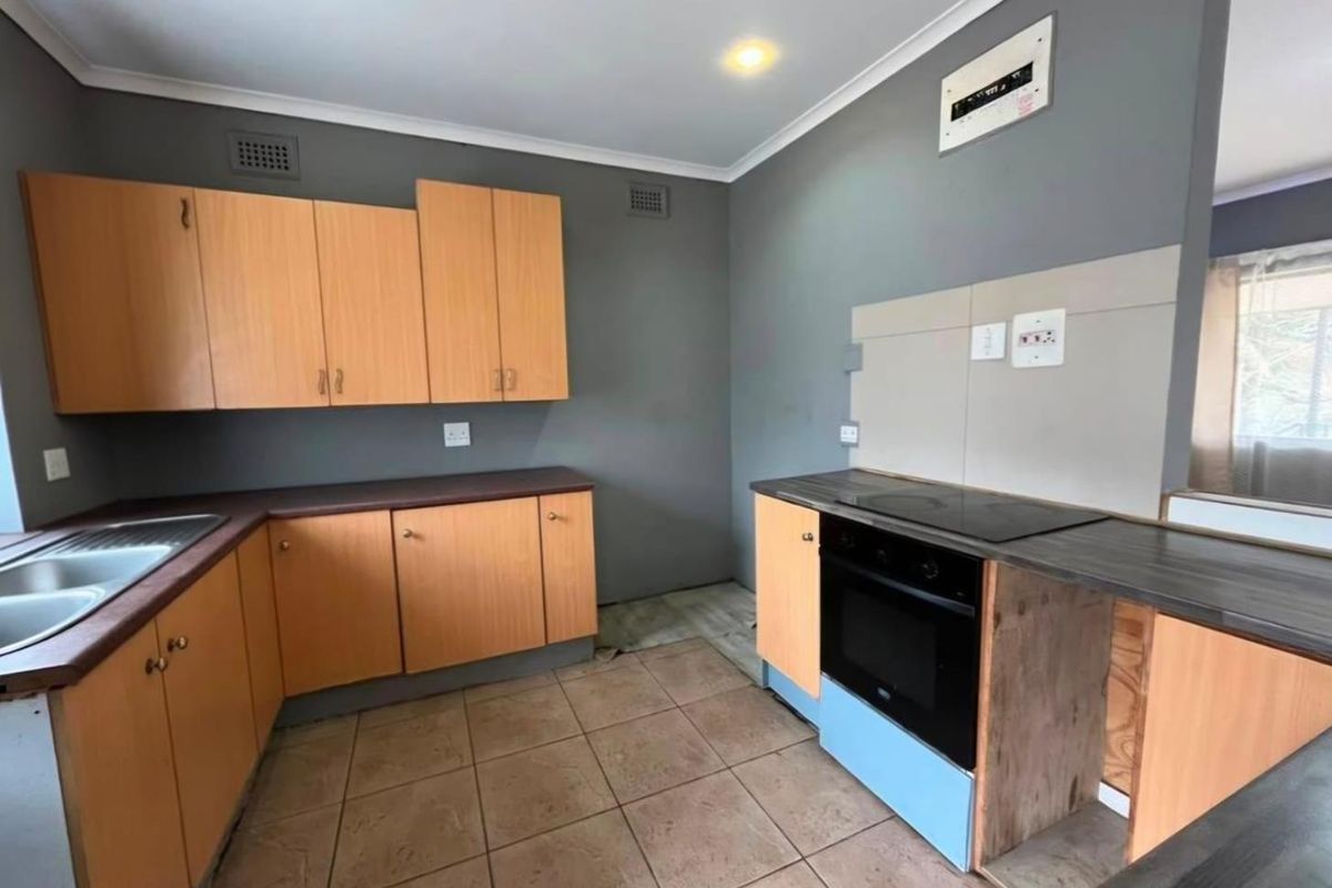 A functional kitchen featuring wood-finish cabinetry, laminate countertops, and built-in cooking appliances, requiring minor finishing touches to the cabinetry base.