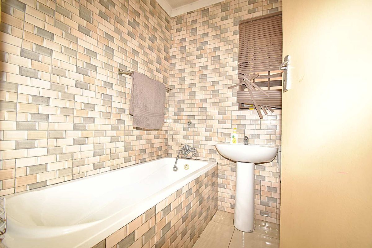 A compact bathroom featuring a built-in bathtub, pedestal sink, and full-height decorative wall tiling.