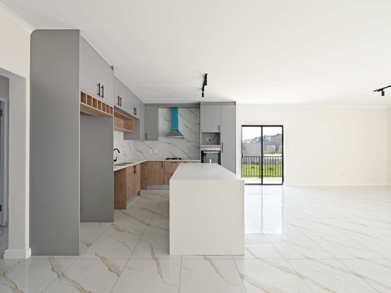 Modern open-plan kitchen featuring a central island, marble-look tiled floors, and sleek cabinetry, flowing seamlessly into a bright living area with garden access.