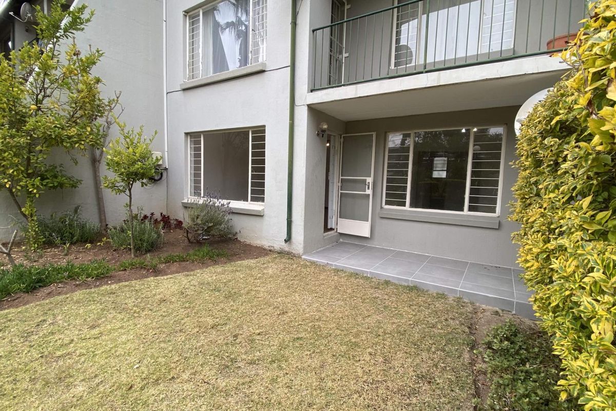 Rear view of the apartment featuring a small tiled patio, a private garden area, and an upper-level balcony with metal railings.