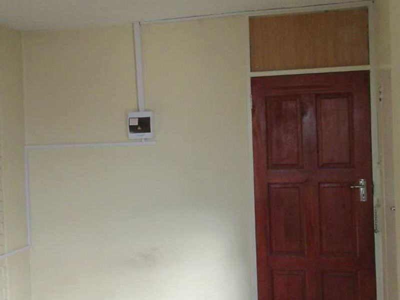 A simple entry area featuring dark tiled flooring and a traditional timber door, with visible surface-mounted electrical conduit along the wall.