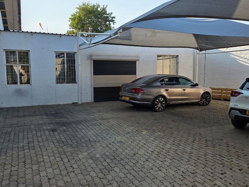 Industrial exterior front featuring a paved driveway, roller shutter door, and a shade sail structure for vehicle parking.