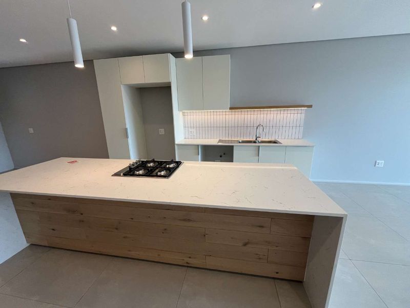 Modern open-plan kitchen featuring a large island with a built-in gas hob, quartz countertops, sleek cabinetry, and contemporary pendant lighting.