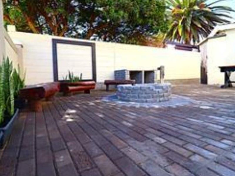 Outdoor patio area featuring brick paving, a built-in braai, and a central stone fire pit, enclosed by a boundary wall.