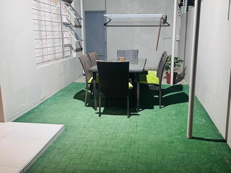 A covered outdoor patio area featuring artificial grass flooring, wall-mounted air conditioning, and security features including window bars and electric fencing.