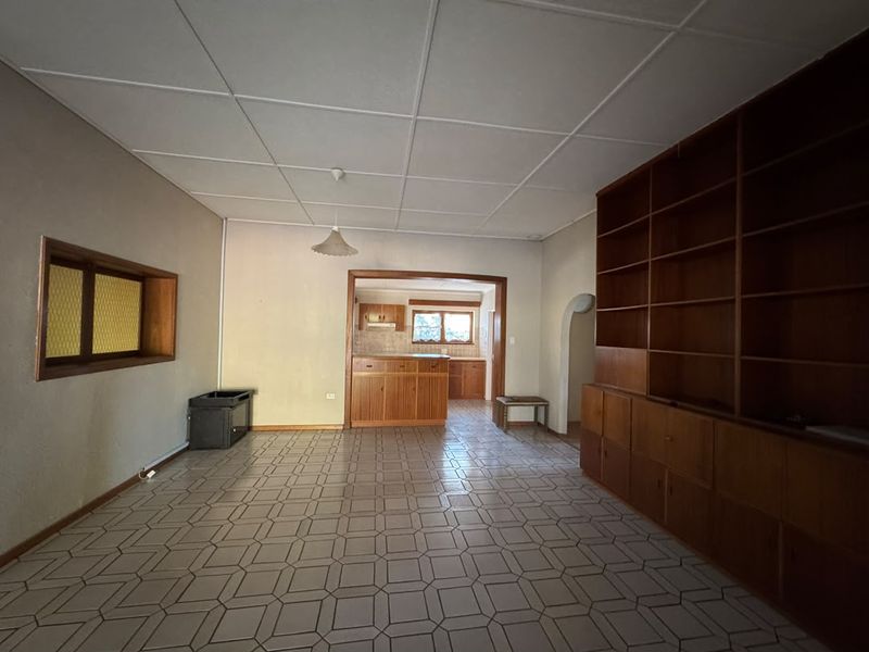 Spacious open-plan living area featuring built-in wooden shelving, tiled flooring, and a view through to the kitchen area.