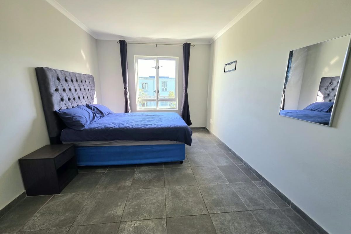 A well-lit bedroom featuring neutral walls, grey tiled flooring, and a window providing natural light.