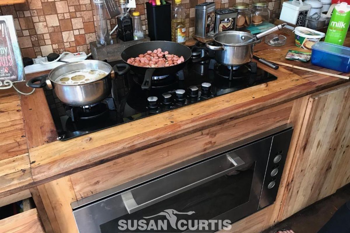 A kitchen workspace featuring a built-in stainless steel oven and a black glass gas hob set into a rustic wooden countertop.