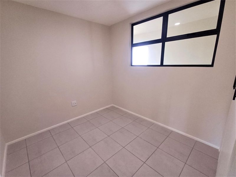 A clean, empty bedroom featuring neutral tiled flooring and a modern black-framed window, providing a bright and versatile space.
