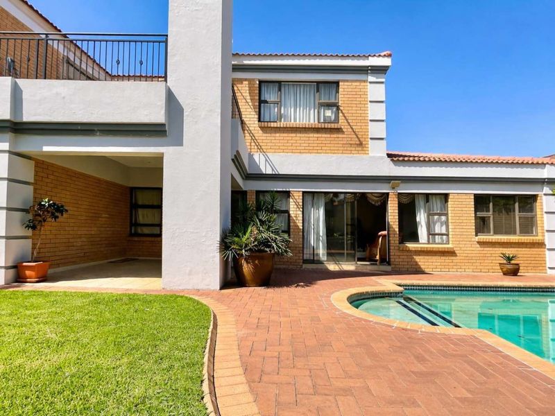 Rear view of the property featuring a swimming pool, brick-paved patio area, covered terrace, and a balcony with wrought iron railings.