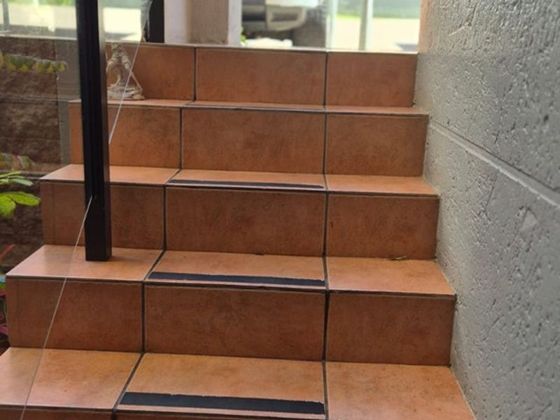 An exterior staircase featuring terracotta-style tiles, a modern glass balustrade with a metal handrail, and integrated anti-slip treads for safety.