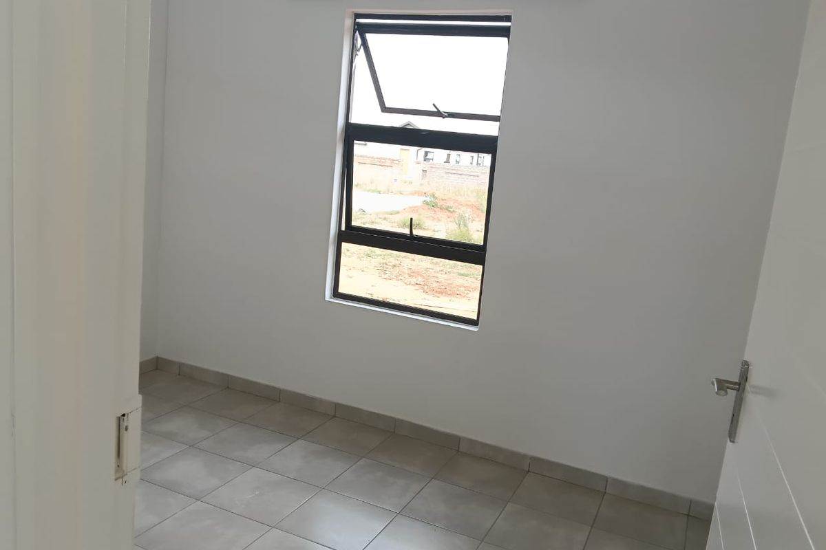 A clean, empty bedroom featuring neutral tiled flooring and a modern aluminium-framed window, providing a blank canvas for interior design.