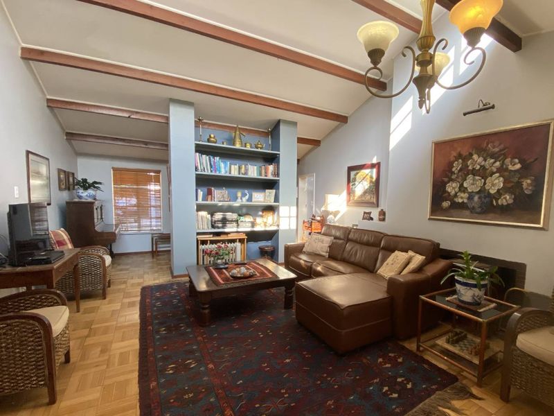 Spacious living room featuring exposed timber ceiling beams, classic parquet flooring, a central built-in shelving unit, and a fireplace.