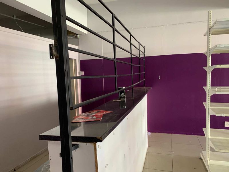 Interior retail space featuring a built-in service counter with a metal security grille, tiled flooring, and wall-mounted shelving units.