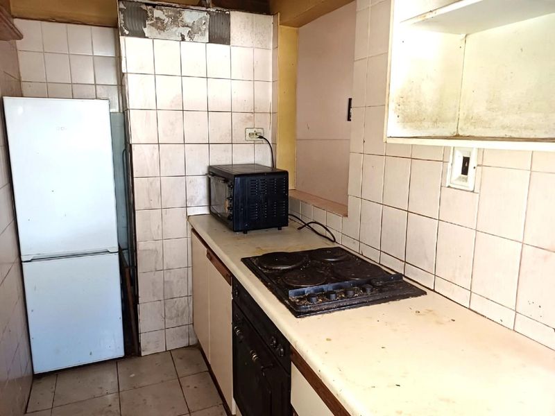 A dated kitchen featuring built-in cabinetry, an electric hob, and an oven, requiring significant renovation and cosmetic updates to improve functionality and aesthetic appeal.
