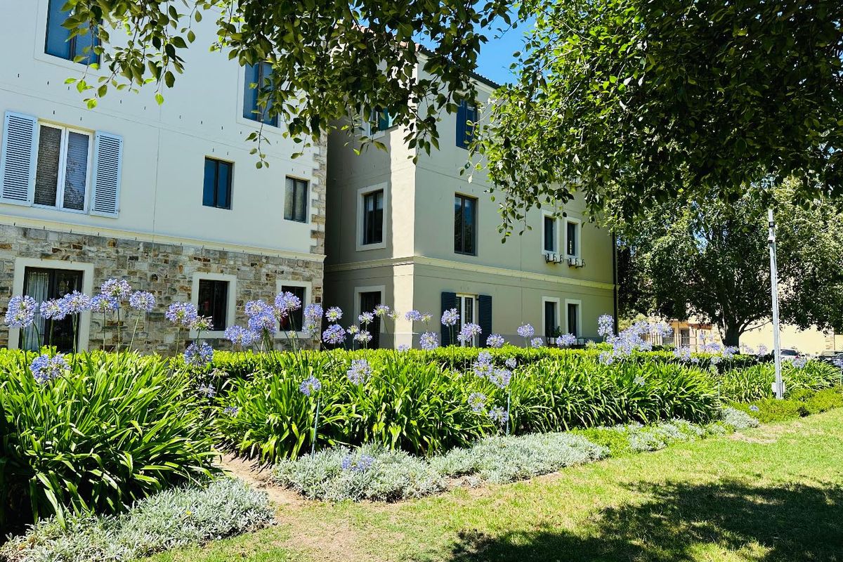 A view of the apartment building exterior featuring stone cladding, window shutters, and a well-maintained landscaped garden area.