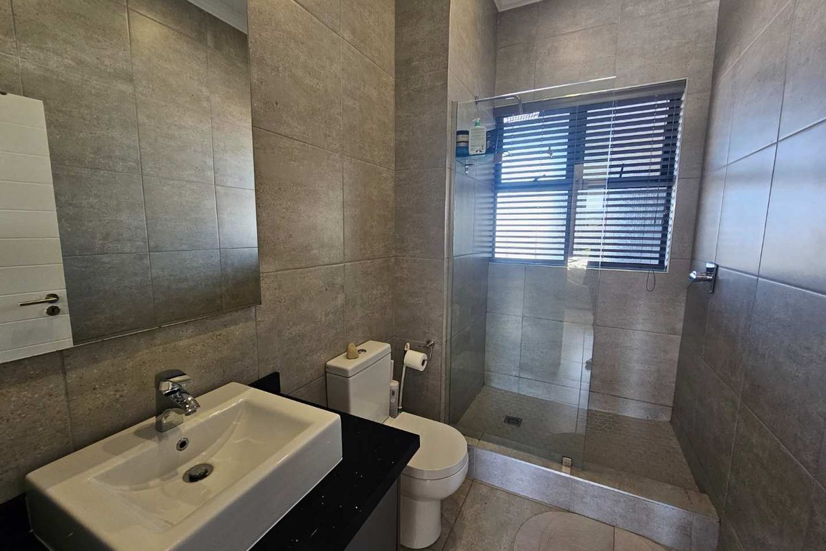 Modern bathroom featuring floor-to-ceiling grey tiling, a floating vanity with a black countertop, a glass-enclosed walk-in shower, and a wall-mounted mirror.