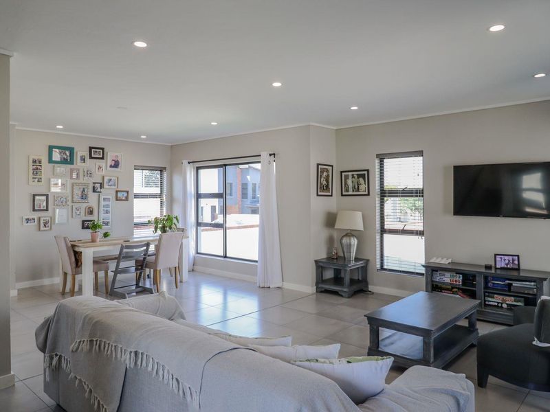 Spacious open-plan living and dining area featuring neutral wall tones, large windows with venetian blinds, and modern tiled flooring throughout.