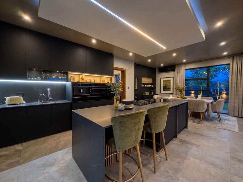Modern open-plan kitchen and dining area featuring sleek dark cabinetry, a large central island with stone countertops, and sophisticated recessed lighting.