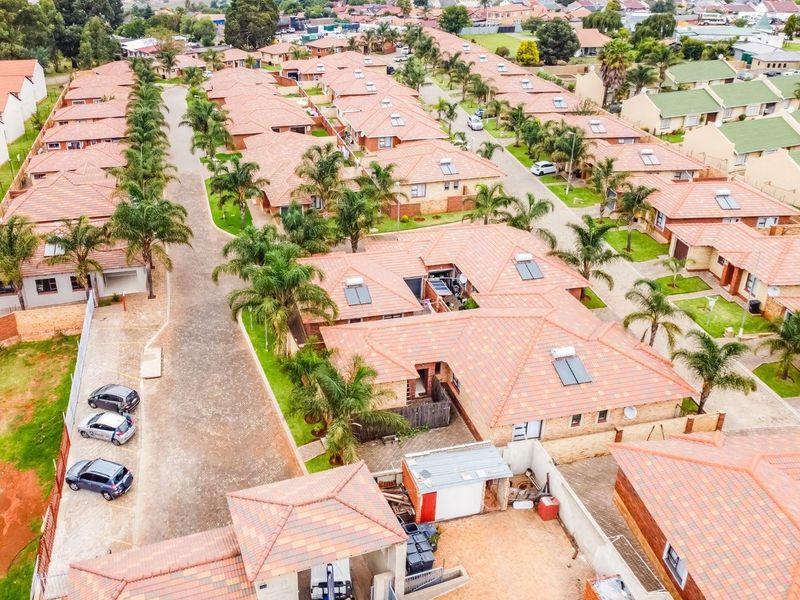 Aerial view of a residential housing complex featuring uniform tiled roof homes, paved driveways, and established landscaping within a secure estate.