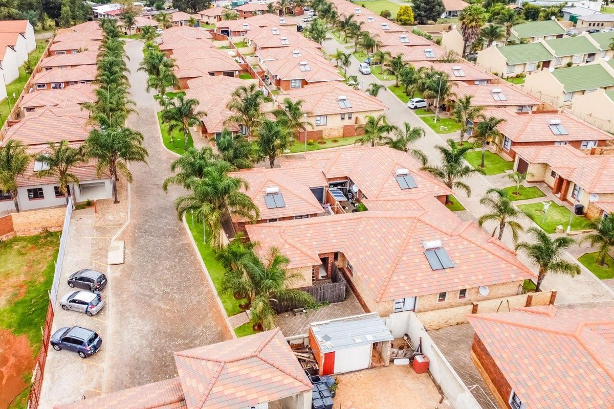 Aerial view of a residential housing complex featuring uniform tiled roof homes, paved driveways, and established landscaping within a secure estate.