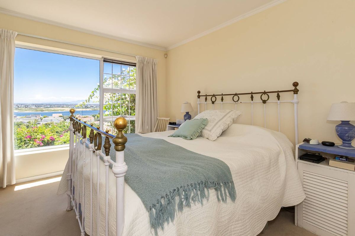 A bright bedroom featuring a large window with scenic water views, neutral wall finishes, and carpeted flooring.