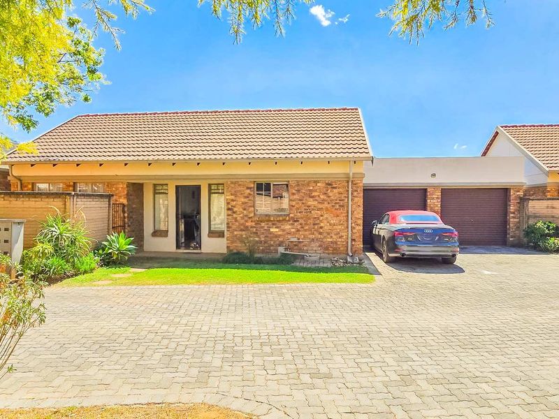 Front elevation of a townhouse featuring a brick facade, tiled roof, and a paved driveway leading to a double garage.