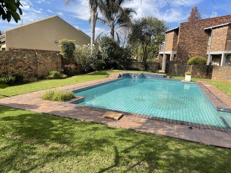 A private backyard featuring a swimming pool with safety net, surrounded by brick paving and established garden landscaping.