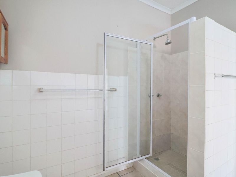 A functional bathroom featuring a walk-in shower enclosure with tiled walls and a wall-mounted cabinet, offering a clean and neutral space.
