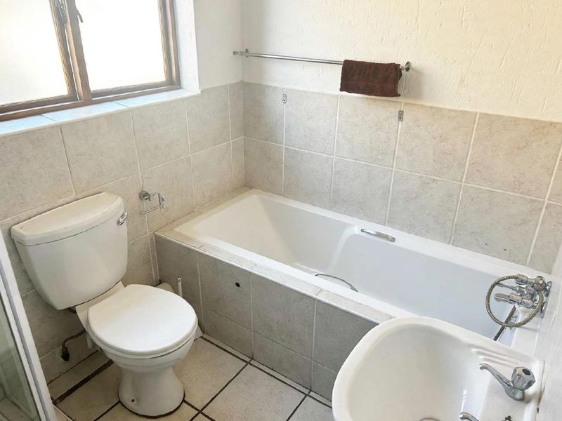 A functional bathroom featuring a built-in bathtub, pedestal basin, and toilet with neutral wall and floor tiling.