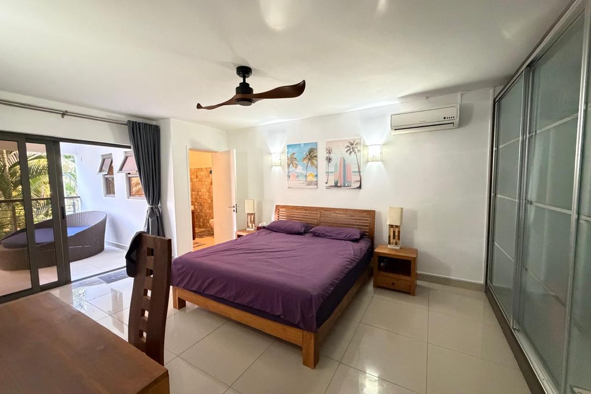 Spacious bedroom featuring tiled flooring, a ceiling fan, wall-mounted air conditioning unit, and large sliding glass doors leading to a private balcony.