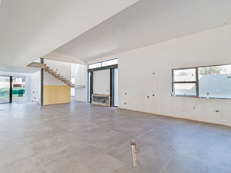 Spacious open-plan living area under construction, featuring large format floor tiles, a modern floating staircase, and expansive sliding glass doors.