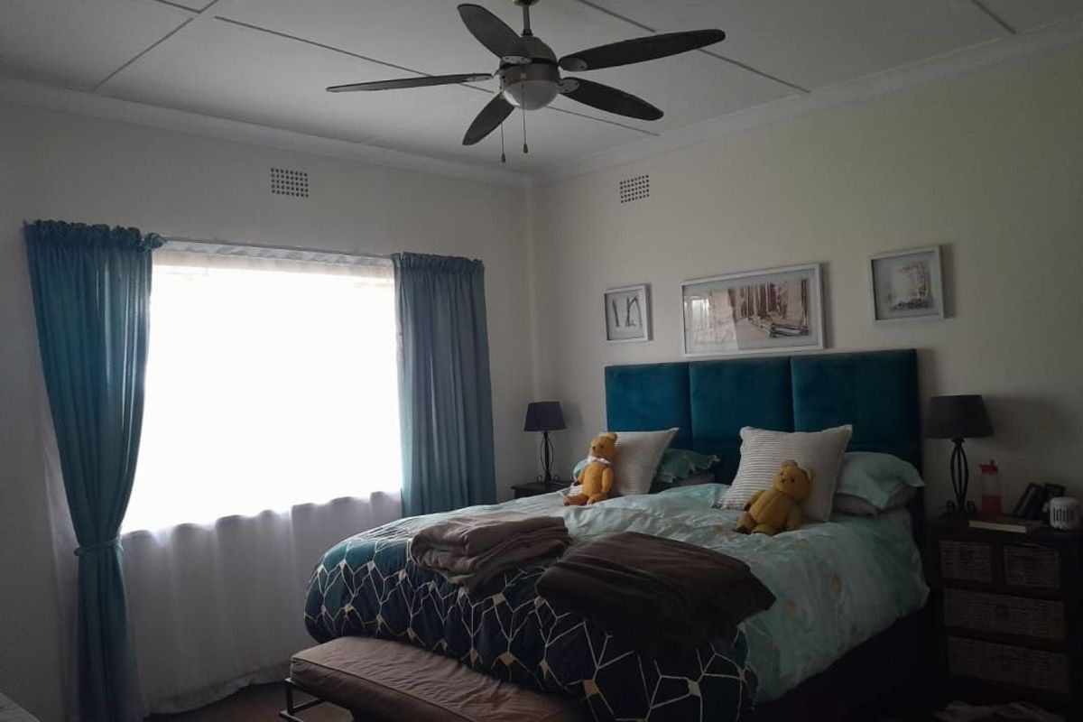 A well-lit bedroom featuring a ceiling fan, tiled ceiling panels, and a large window with curtains.
