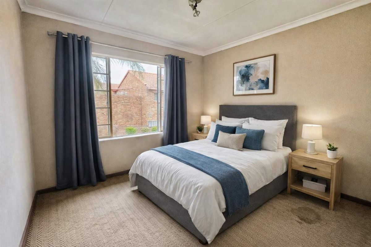 A well-lit bedroom featuring neutral walls, carpeted flooring, and a large window providing natural light.